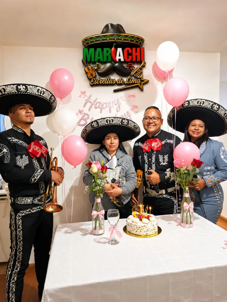 Celebración íntima en casa con torta, rosas y el cuarteto con sombreros de charro